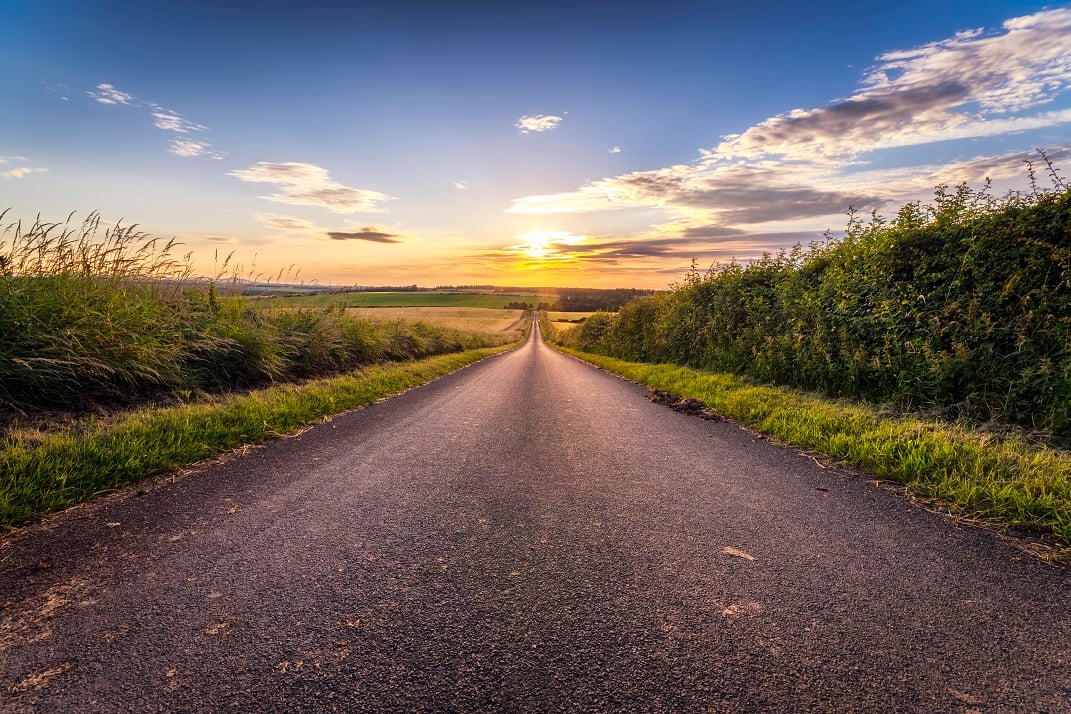 Country road leading to sunset on horizon
