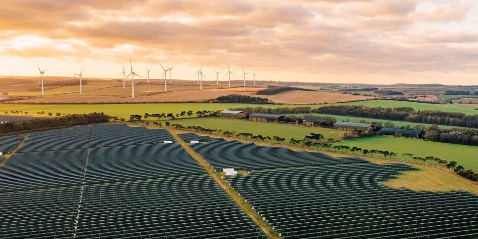 Solar panels in field with wind turbines on horizon